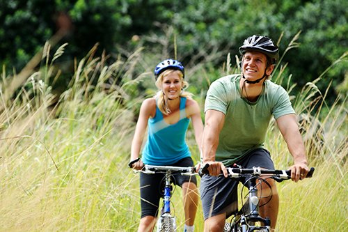 Two people are riding bikes through a field of tall grass.